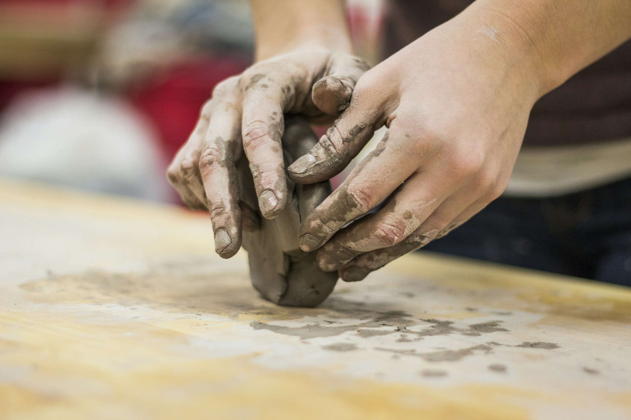Clay-covered hands shaping a ceramic form.